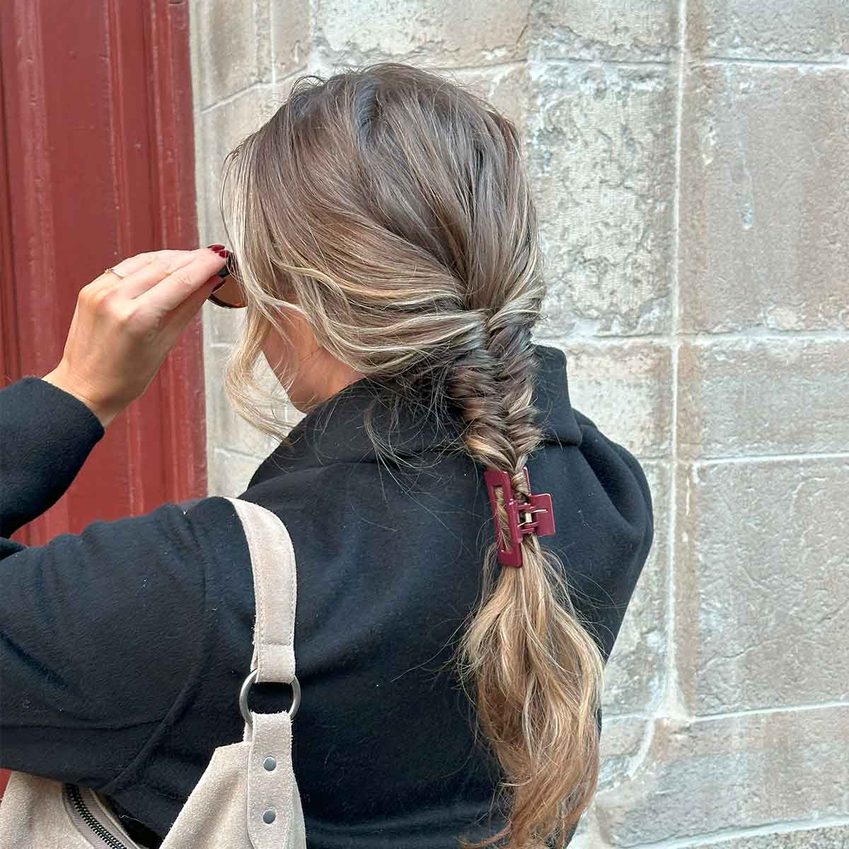 Eine glänzende burgunderrote Haarspange in einem geflochtenen braunen Haar.